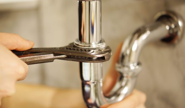 Plumbing repair service. Professional installer with spanner checking pipe.